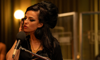 Szenenbild aus dem Film "Back to Black": Die Sängerin Amy Winehouse, dargestellt von Marisa Abela, steht in einem Tonstudio vor einem Mikrofon und singt. Sie hält sich einen Kophörer an ihr rechtes Ohr. (© Dean Rogers / Focus Features)