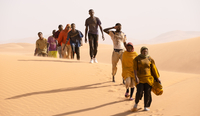 Szenenbild aus dem film "Ich Capitano": Eine Reihe von Schwarzen Frauen und Männern laufen im Gänsemarsch durch eine Wüstenlandschaft. (© Greta De Lazzaris / X Verleih AG)