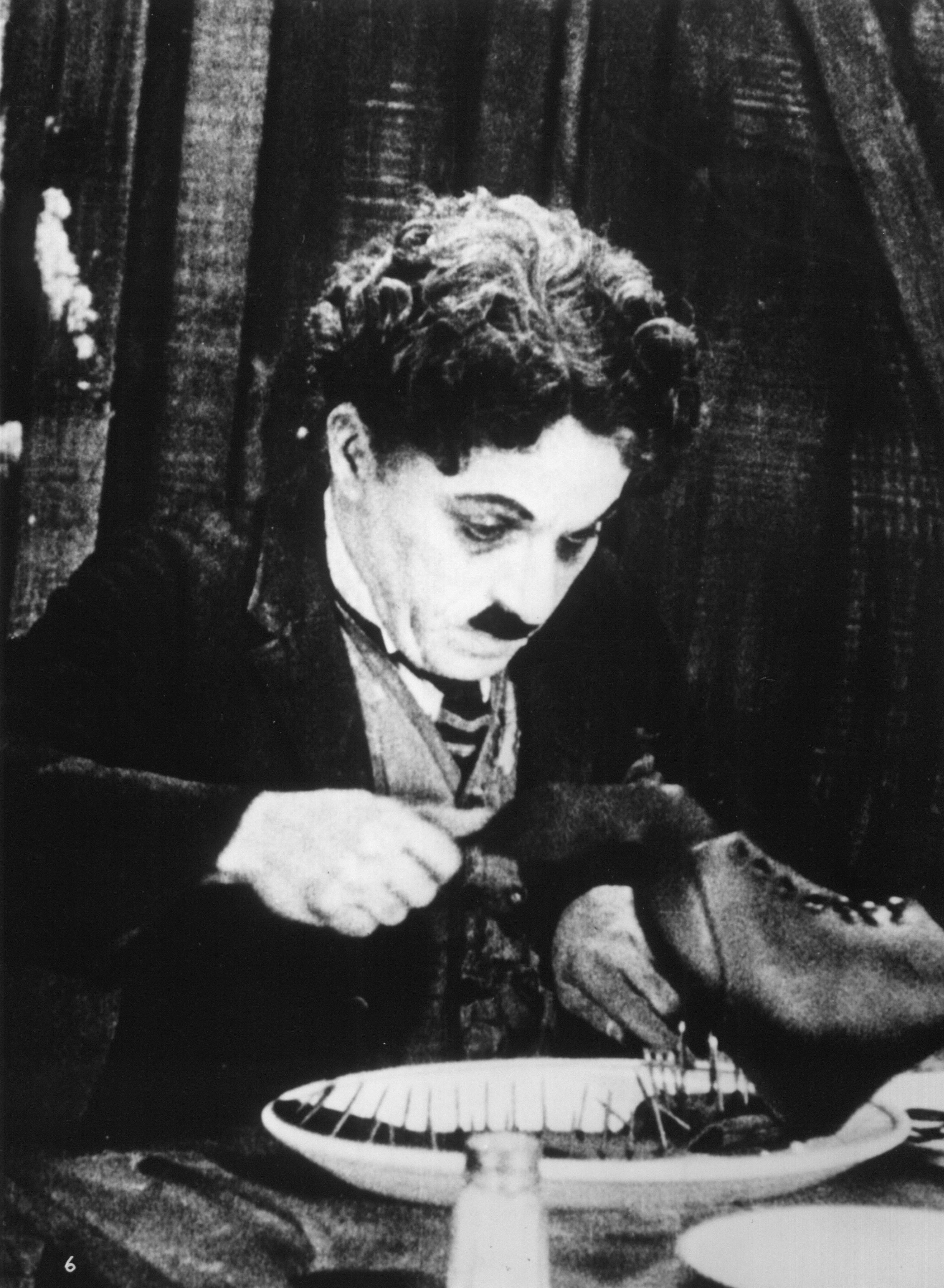 Szenenbild aus dem Stummfilm GOLDRAUSCH: Charlie Chaplin zerteilt mit Messer und Gabel einen Schuh