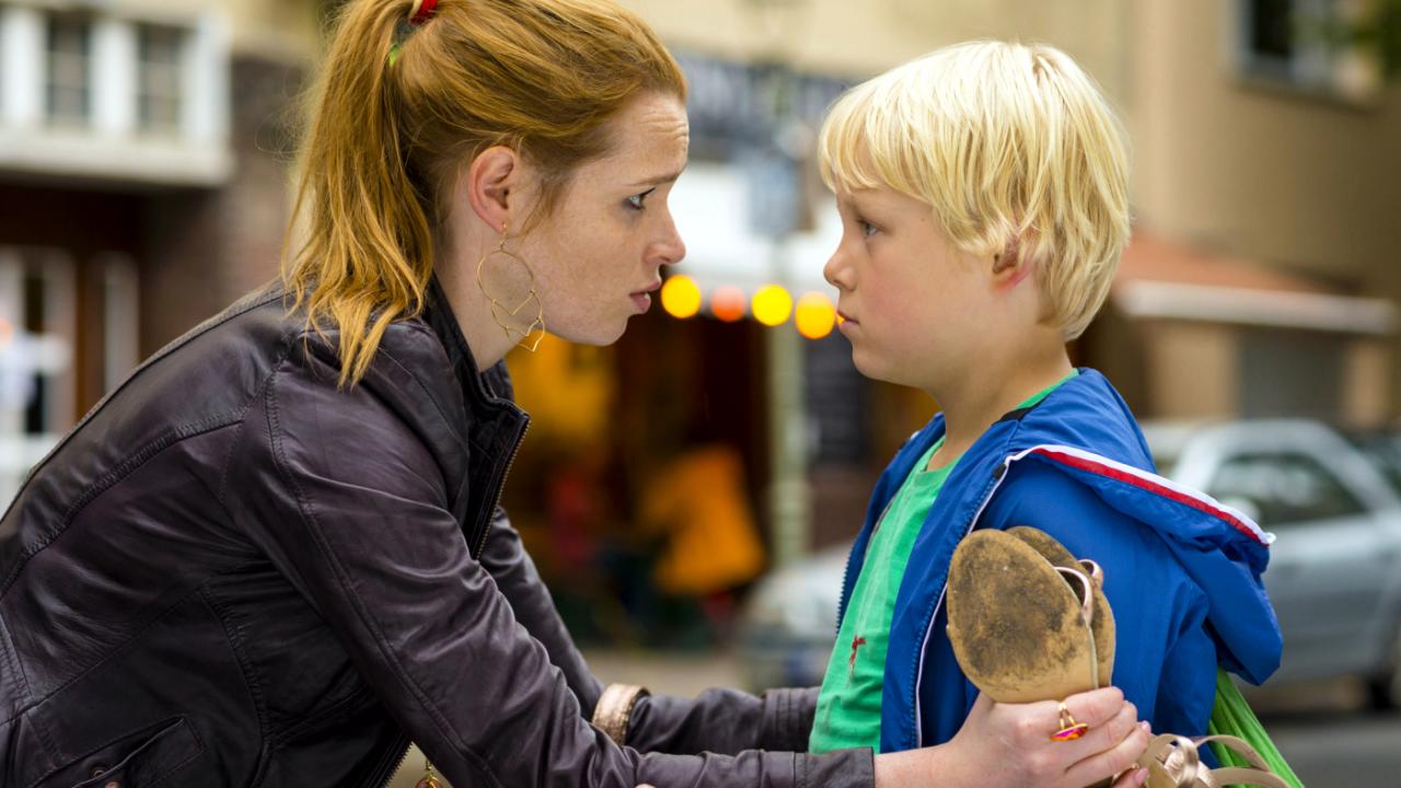 Szenenbild aus dem Film "Rico, Oskar und die Tieferschatten": Nahaufnahme: Eine junge Frau mit Pferdeschwanz beugt sich leicht zu einem blonden Jungen herunter und hält ihn an den Armen fest.