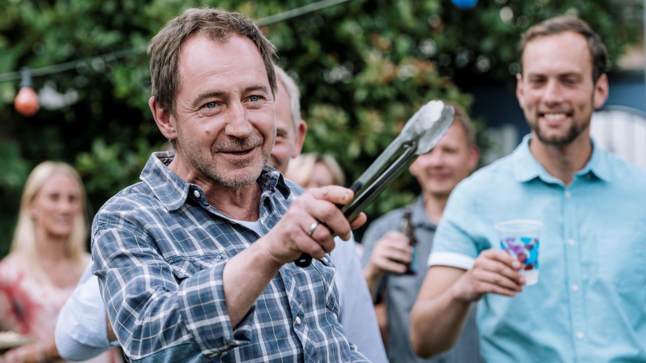 Frank Pielke gestikuliert mit einer Grillzange in der Hand während eines Grillfests im Garten.