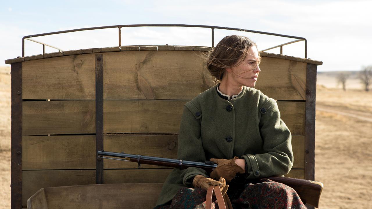 Szenenbild aus dem Western "The Homesman": Eine Siedlerin sitzt auf einem Kutschenwagen, hält Zügel und ein Gewehr in den Händen.