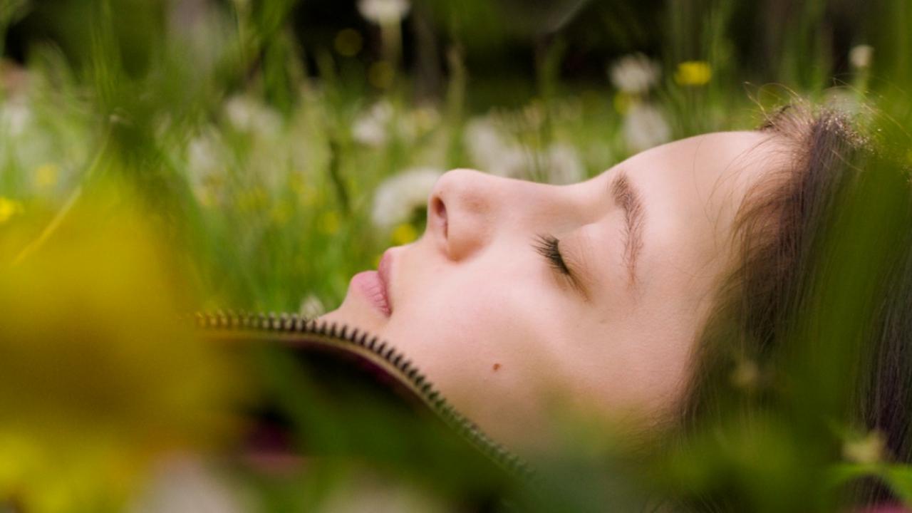 Nahaufnahem im Profil: Ein junges Mädchen mit heller Haut und braunen Haaren liegt mit geschlossene Augen auf einer Blumenwiese