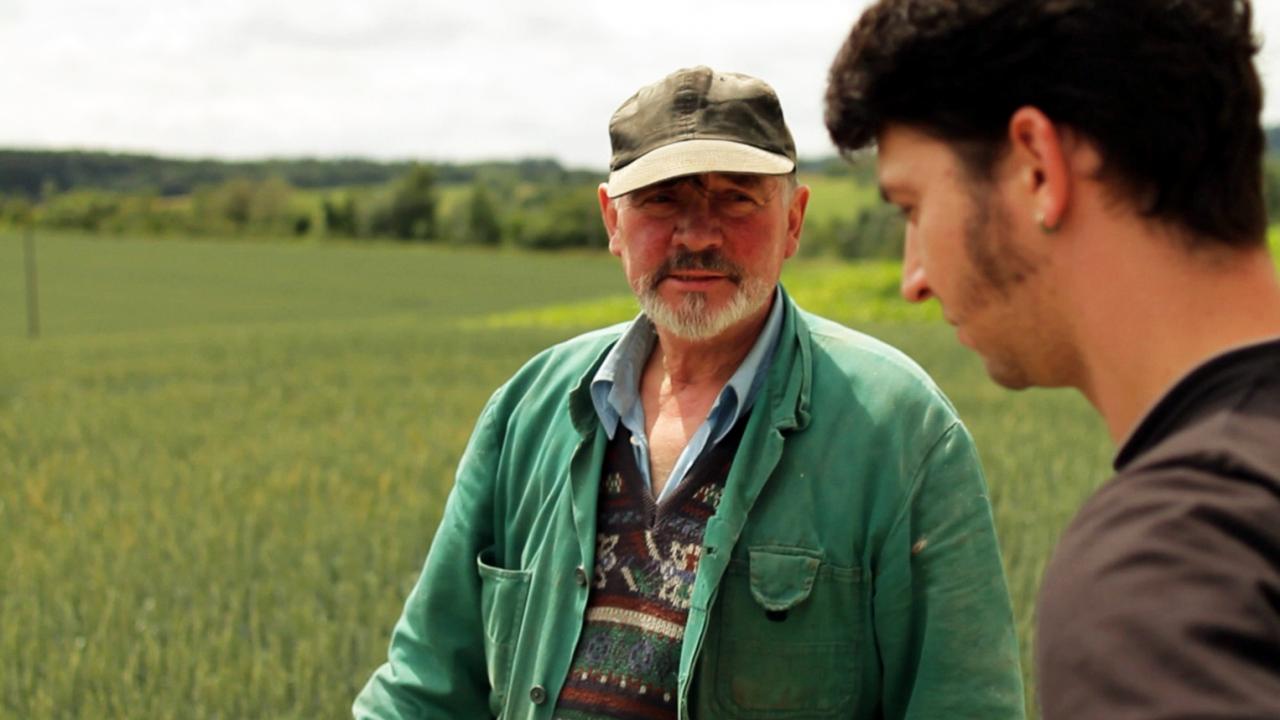 Szenenbild aus dem Dokumentarfilm "Sauacker": Ein junger Mann und ein älterer Mann stehen auf einem Feld.