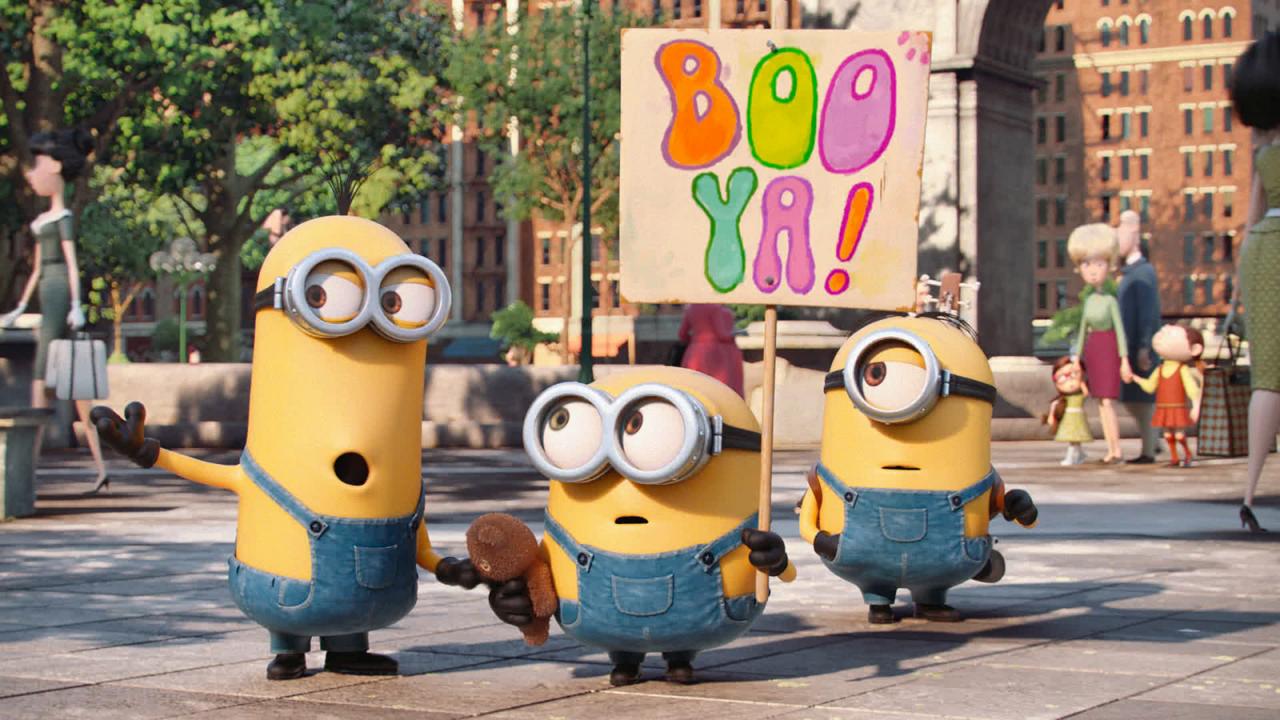 Drei Minions stehen in einer Stadt, einer hält ein Schild mit "Boo Ya!" darauf. Menschen gehen im Hintergrund vorbei.