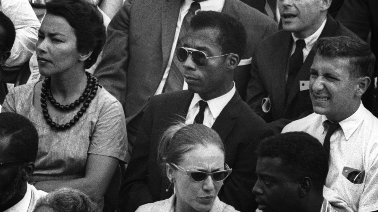 Schwarz-weiß-Foto von Menschen in formeller Kleidung bei einer Versammlung, Schwarzer Mann mit Sonnenbrille in der Mitte.