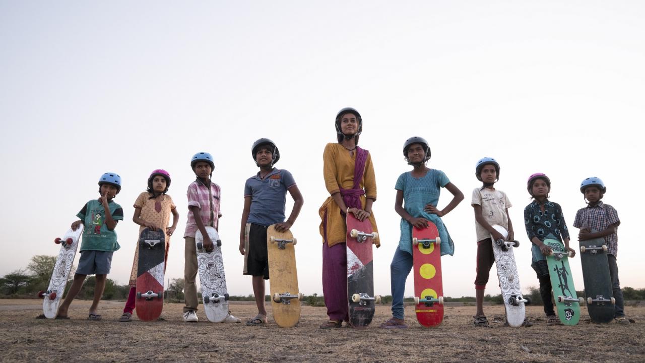 Indische Mädchen und Jungen stehen nebeneinander und präsentieren ihr Skateboard.