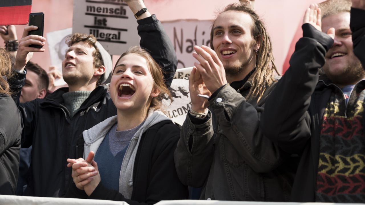 Eine junge Frau, umringt von anderen Leuten ihres Alters, klatscht auf einer Demonstration.