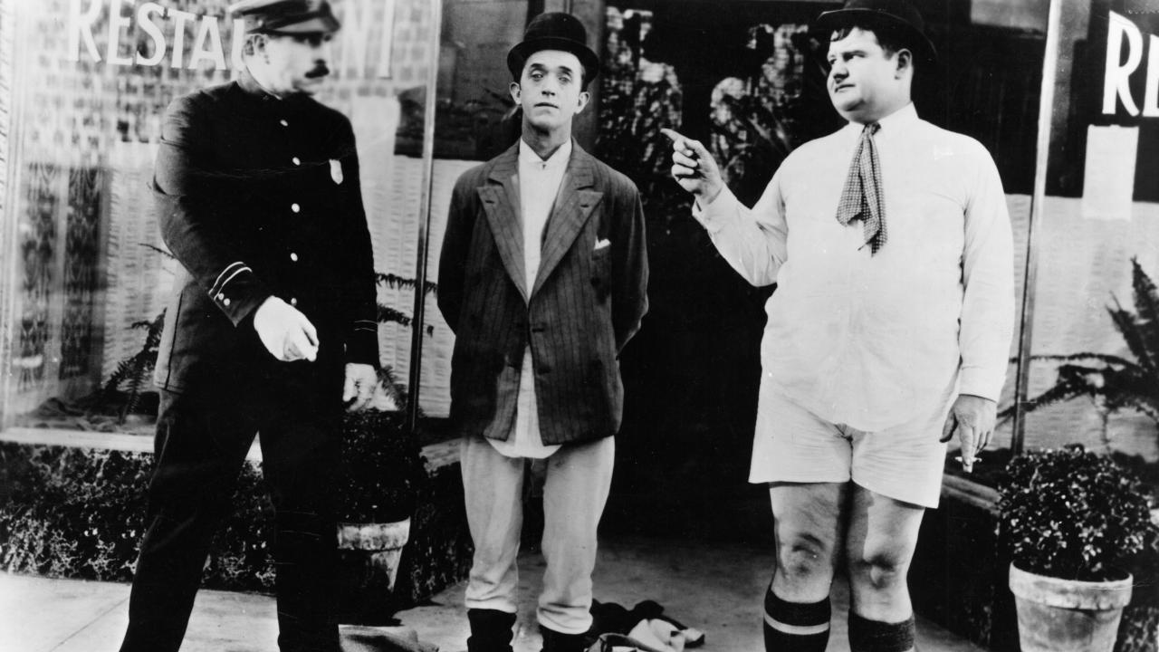 Szenenbild aus der Slapstick-Komödie DER BELEIDIGTE BLÄSER: Die Komiker Laurel und Hardy stehen in Unterhosen auf der Straße neben einem Polizisten.