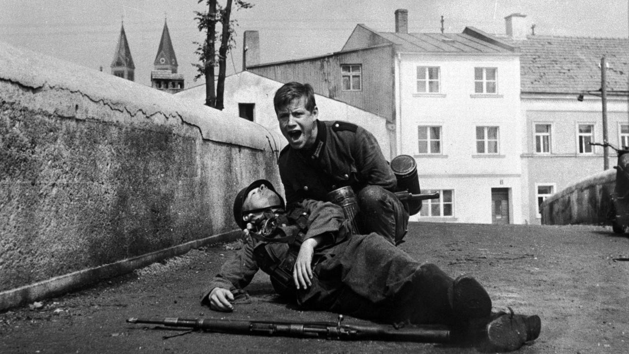 Szenenbild aus dem Antikriegsfilm DIE BRÜCKE: Ein Jugendlicher hält auf einer Brücke schreiend einen jungen, toten Soldaten im Arm.