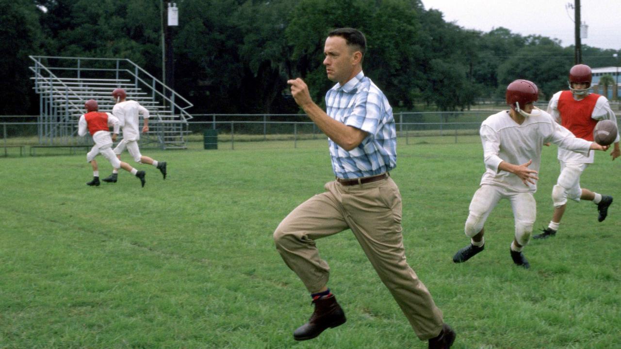 Szenenbild aus dem Film FORREST GUMP: Ein Mann rennt zielstrebig von rechts nach links über ein American-Football-Feld. Neben ihm und im Hintergrund sind Football-Spieler zu sehen.-