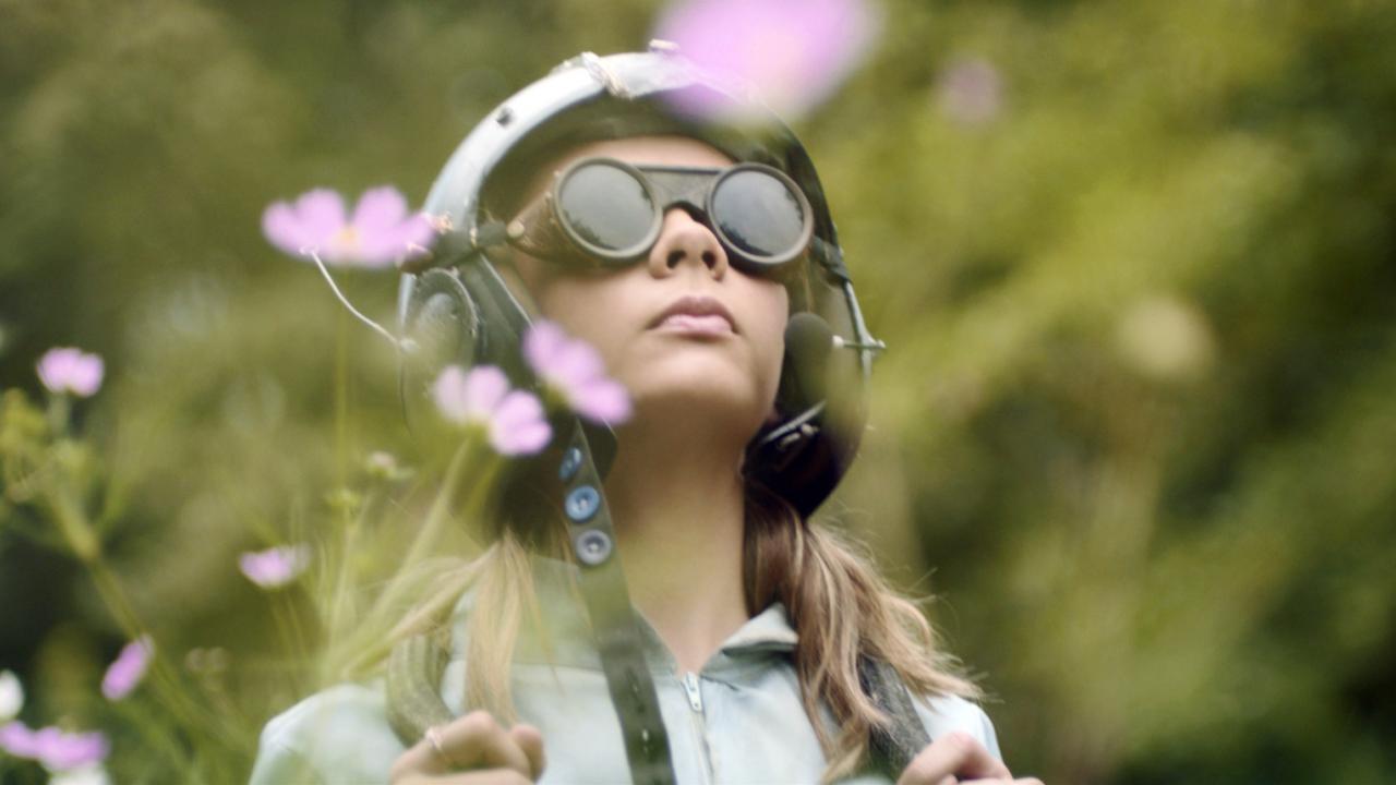 Erdmännchen und Mondrakete, Szenenbild: Ein Mädchen mit Helm und Sonnenbrille steht inmitten in einer hohen Blumenwiese.