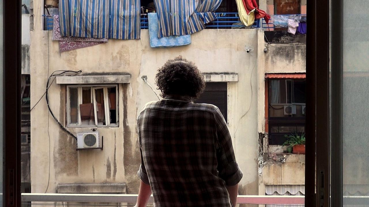 Haunted, Szenenbild: ein Mann, Rücken zu Kamera, lehnt sich aus dem Fenster. Vor ihn eine Fassade von Fenster und Balkons mit hängender Wäsche und schmutzige Wände. 