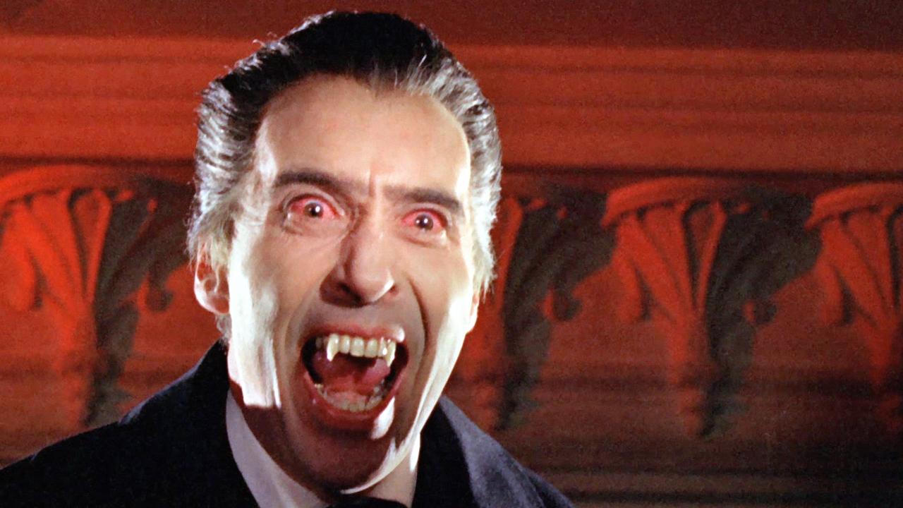 Szenenbild aus dem Film DRACULA (1958): Christopher Lee als Vampir Count Dracula. Er reißt seinen Mund auf und hat rot unterlaufene Augen. Der Hintergrund ist rote Wand mit Stuck zu sehen.