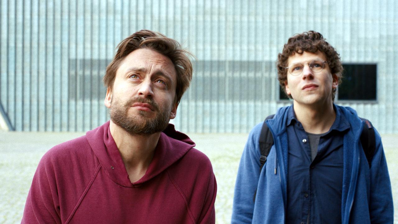 Szenenbild aus dem Drama A REAL PAIN: Zwei junge Männer (Kieran Culkin und Jesse Eisenberg) stehen vor etwas außerhalb des Bildes und schauen nach oben. Im Hintergrund ist die Wand zu sehen.