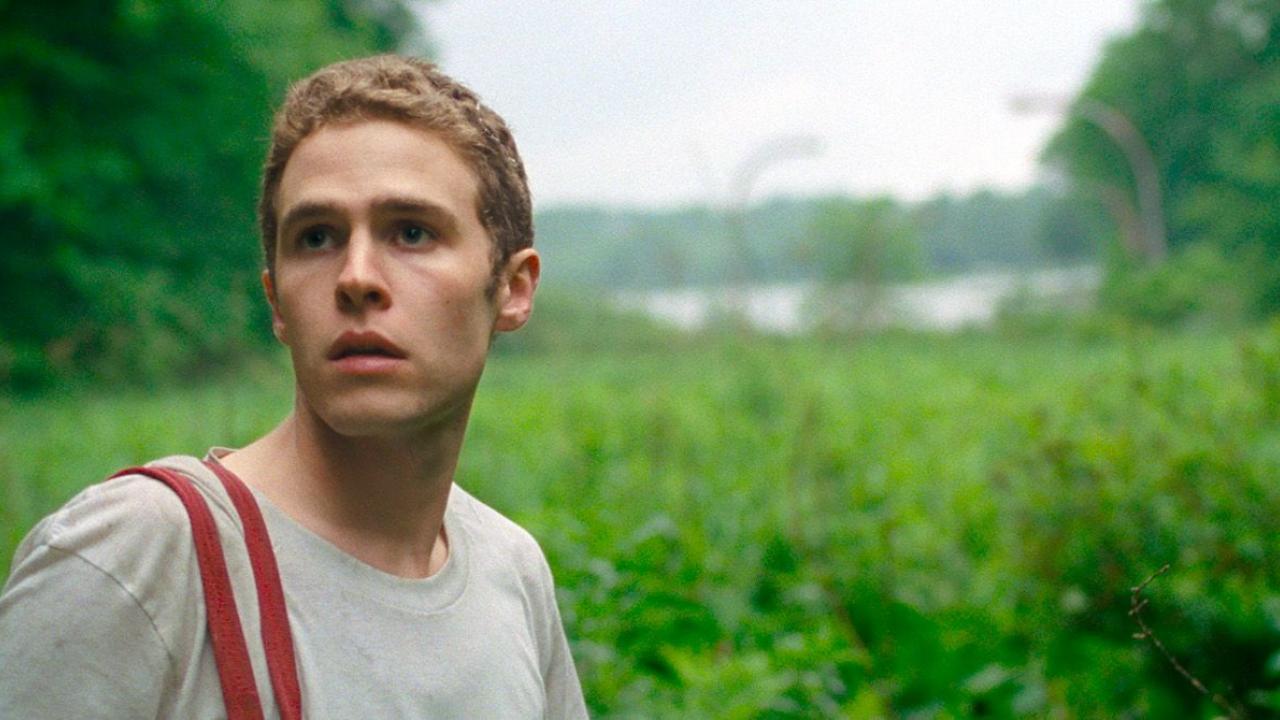 Lost River, Szenenbild: ein junger Mann im T-shirt guckt verwundert. Im Hintergrund eine grüne Naturlandschaft.