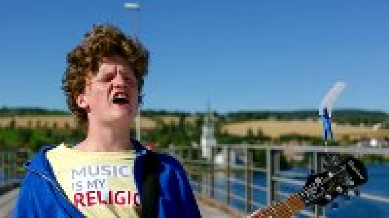 Thilda & die beste Band der Welt, Szenenbild: Nahaufnahme des rothaarigen Lockenkopfs Aksel, der auf einer Brücke steht und voller Inbrunst singt.