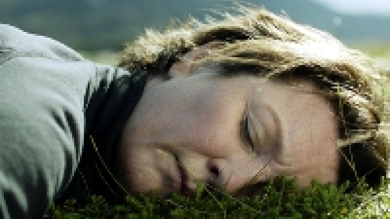 Gegen den Strom, Szenenbild: Nahaufnahmer einer Frau um die 50 mit kurzen Haaren, die wie schlafend auf Gras liegt.