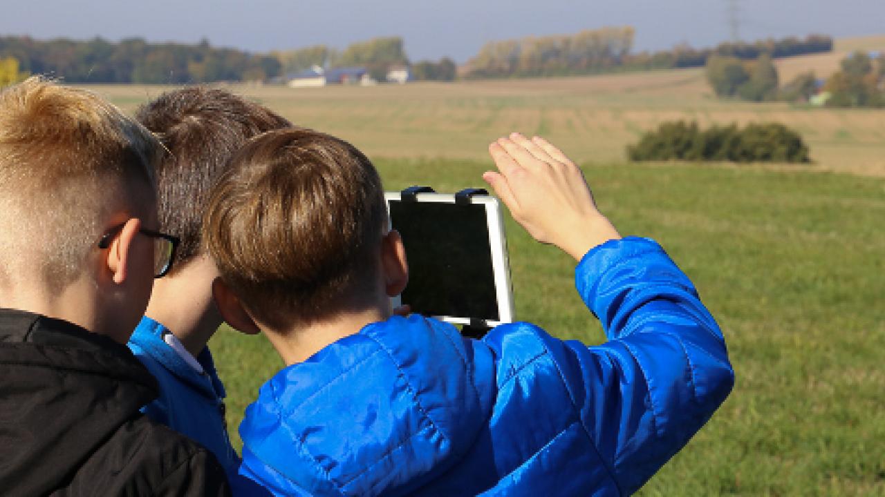 Drei Jungen, die am Projekt FILMmobil teilnehemn, filmen in einer ländlichen Landschaft mit einem Tablet