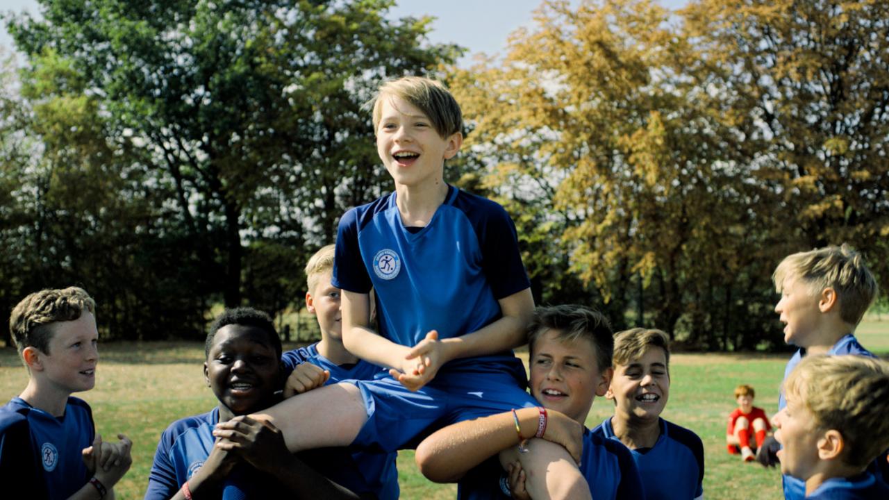 Zu weit weg, Szennebild: Ein Junge in blaune Fußbatrikot wird von seinen jubelnden Teamkameraden auf den Schultern getragen.