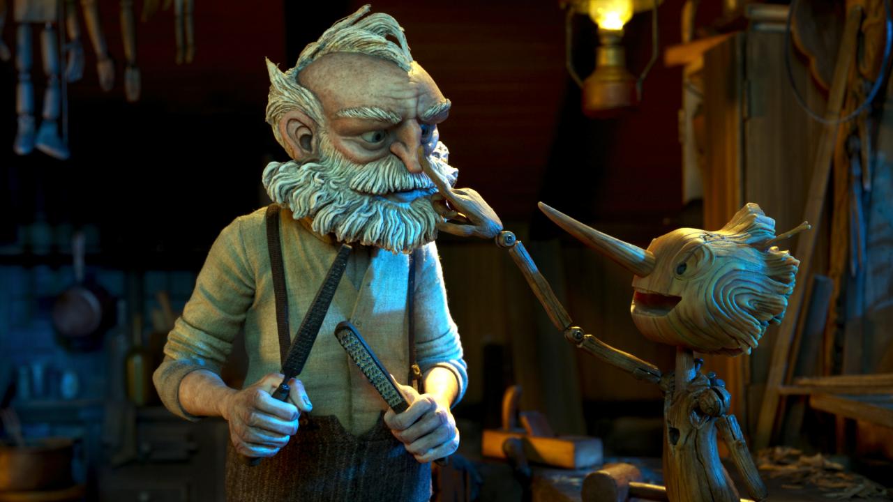 Guillermo de Toros Pinocchio, Szenenbild aus dem Puppenttickfilm: Ein alter Mann mit weißem Bart und einer Holzpfeile in der Hand steht neben einer kindergroßen Holzpuppe mit langer Nase. Sie fässt dem Mann an die Nase.