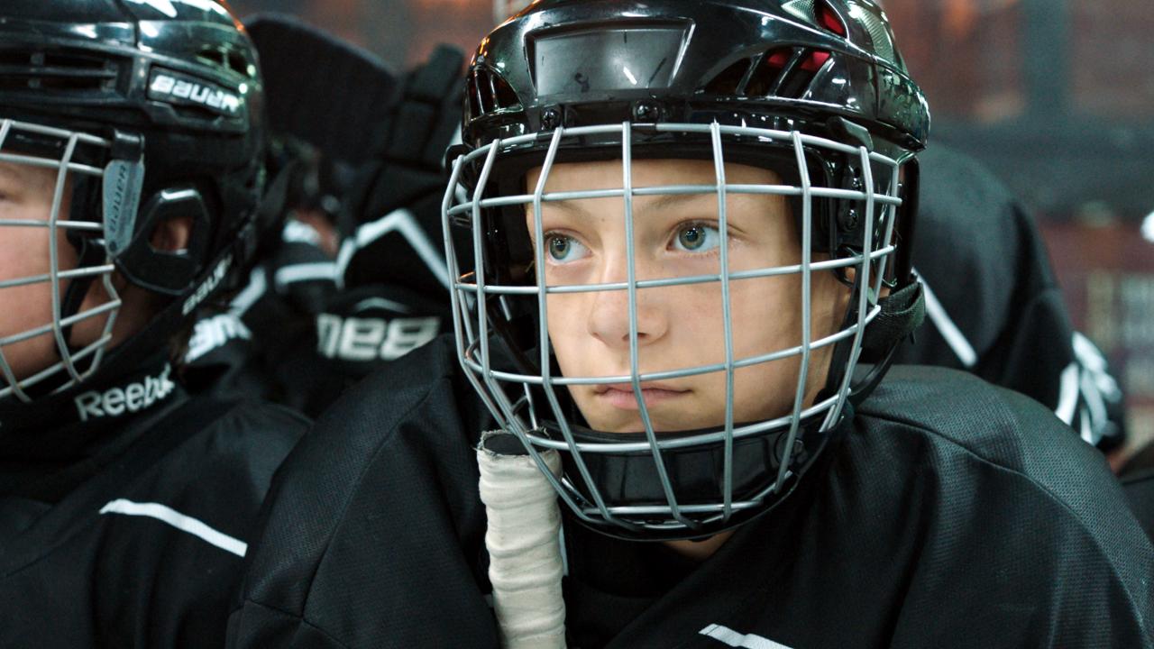 Close, Szenenbild: Nahaufnahme eines Jungen, der einen Eishockey-Helm mit Gitterschutz trägt.