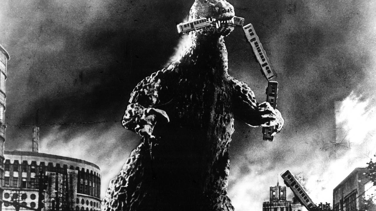 Godzilla, Szenenbild: Ein dinosauriermäßiges, riesiges Monster steht zwischen Häusern und verschlingt einen Eisenbahnzug.