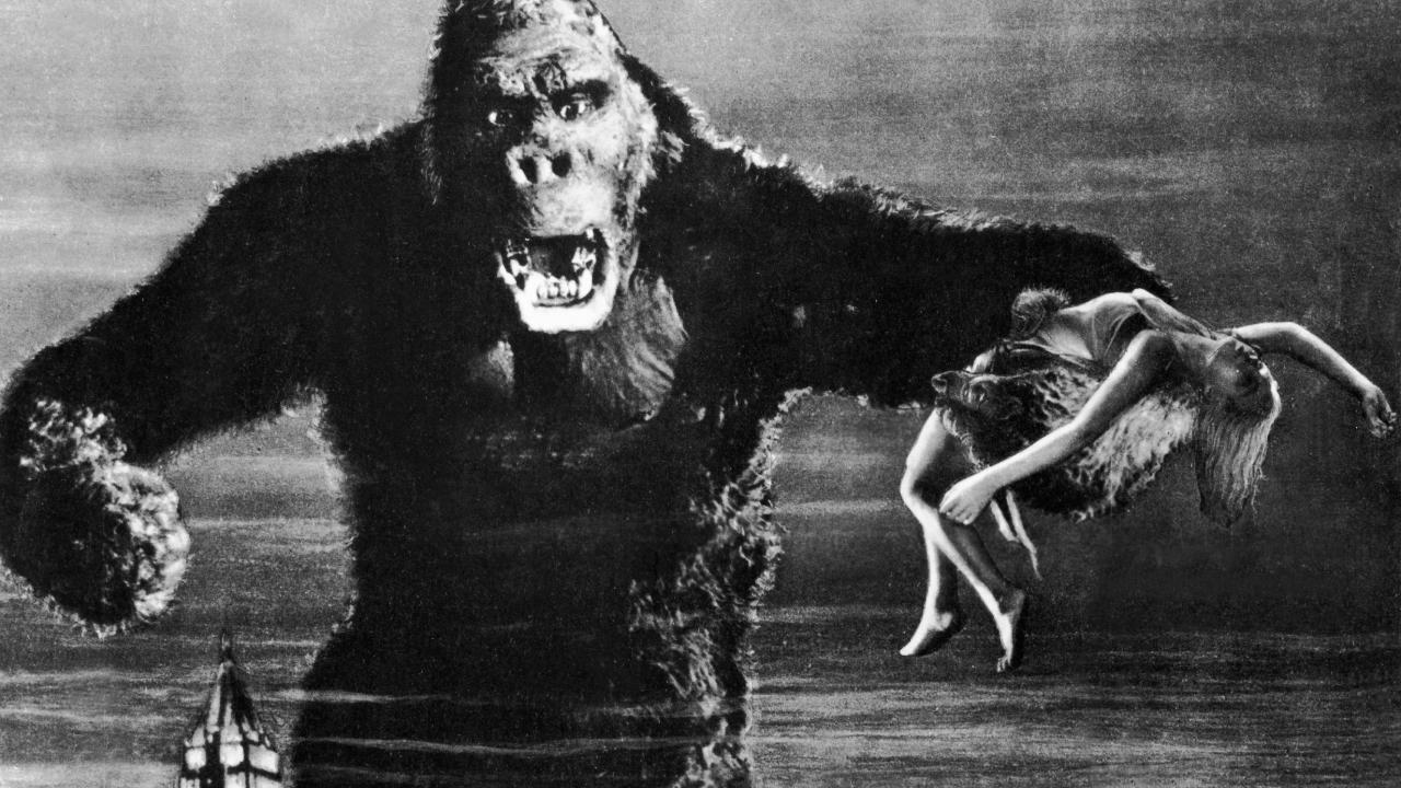 King Kong und die weiße Frau, Szenenbild aus dem Schwarz-Weiß-Film: Ein riesiger, Häuser überragender und bedrohlich aussehender Gorilla hält eine Frau in seiner linken Pranke.