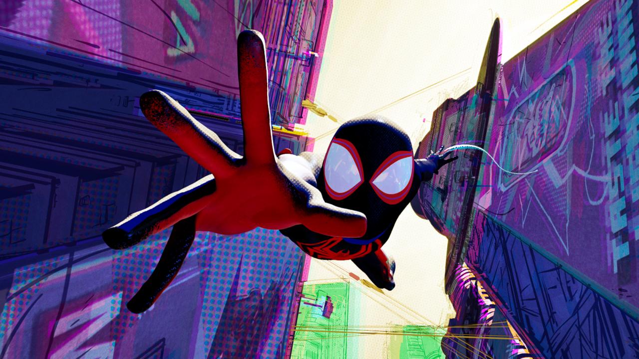 Spider-Man: Across the Spider-Verse, Szenenbild aus dem Animationsfilm: In einer Häuserschlucht, die in der Untersicht zu sehen ist, fliegt der maskierte Spider-Man mit einer ausgestreckten Hand auf den Betrachtenden zu.