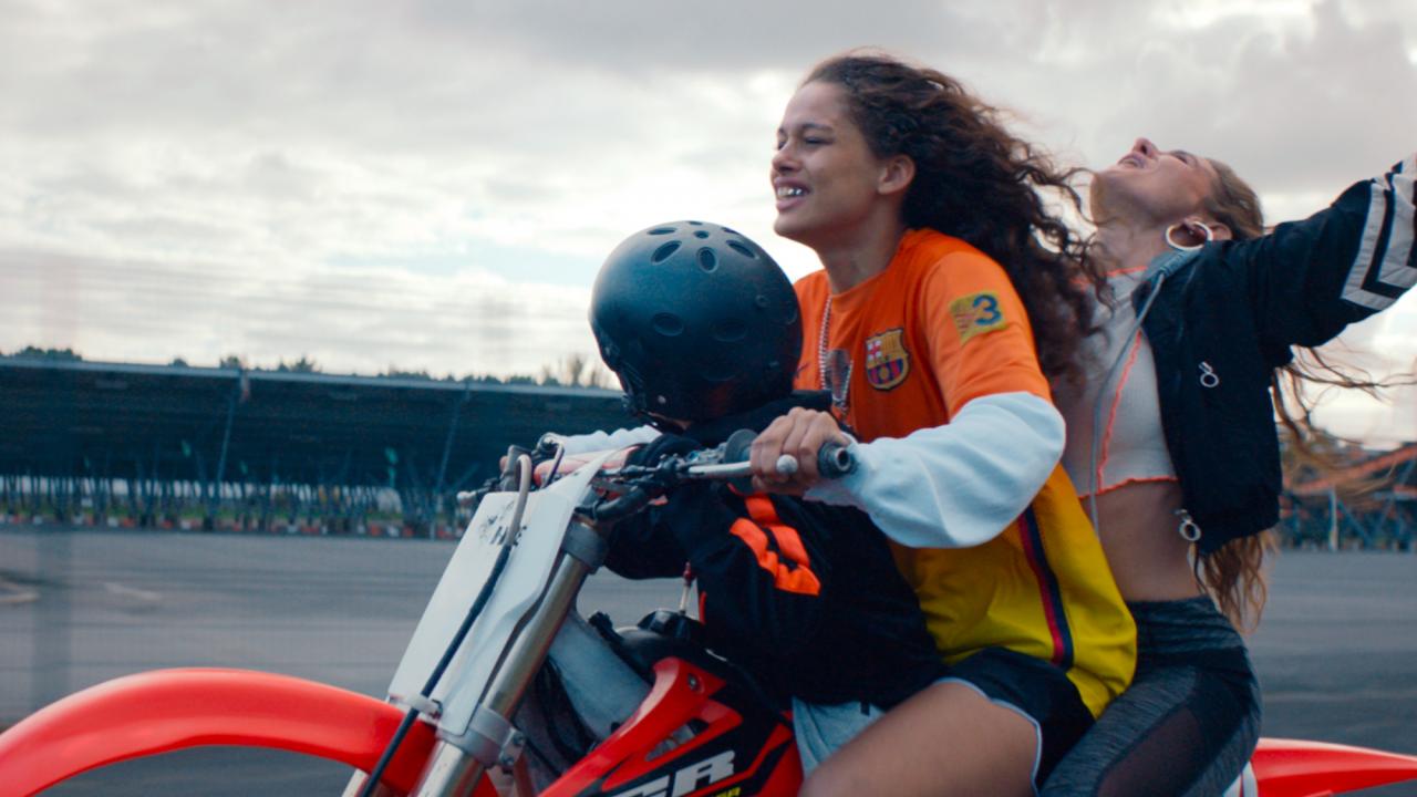 Rodeo, Szenenbild: Zwei junge Frauen und ein Kind sitzen auf einem Motorrad. Die Frau, die hinter der Fahrerin sitzt, reißt ihre Arme in die Höhe. Nur das kleine Kind trägt einen Sturzhelm.