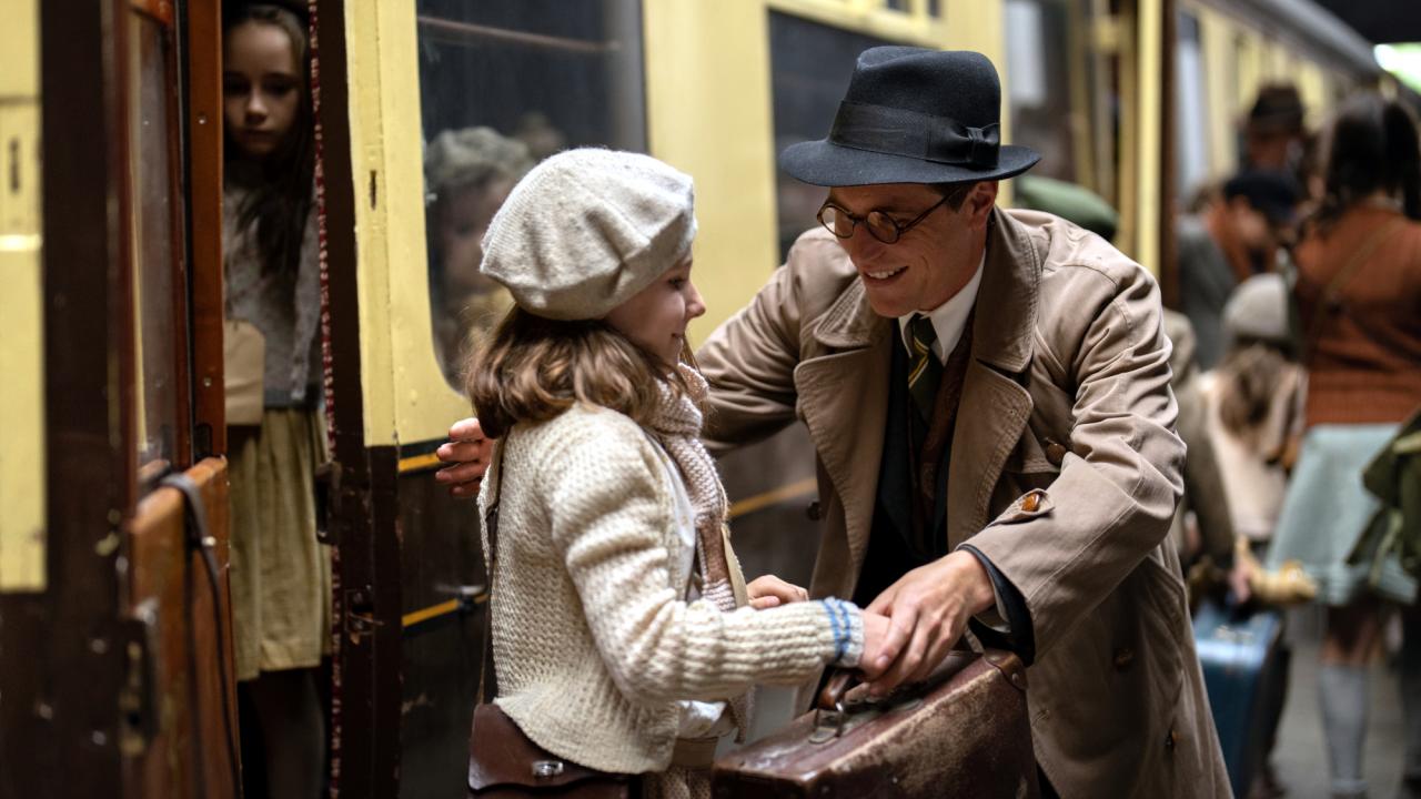 Szenenbild aus dem Film One Life: Ein junger Mann, der im Stil der 1940er-Jahre gekleidet ist, begrüßt auf einem Bahnhof ein kleines Mädchen.