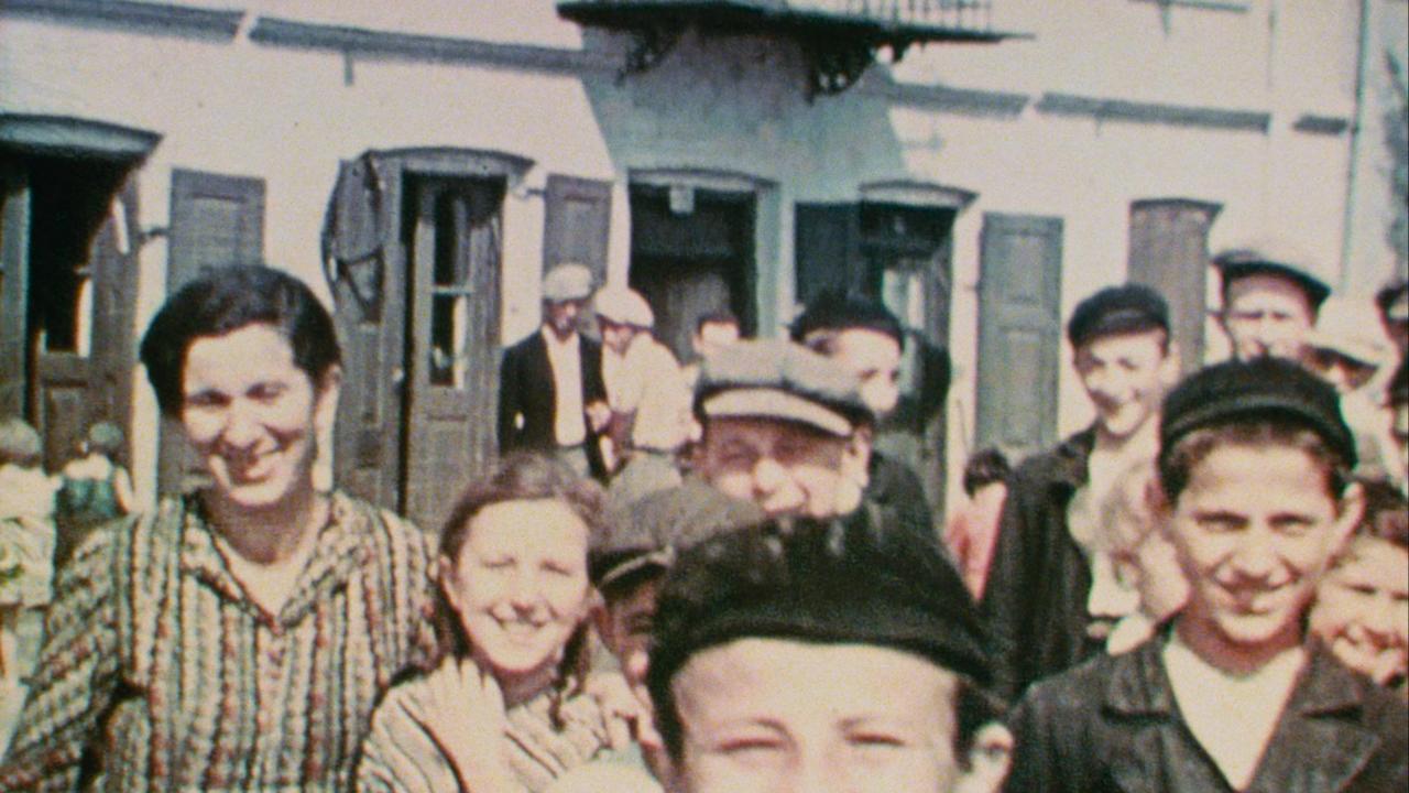 Szenenbild aus dem Film "Three Minutes – A Lengthening": Drei Kinder und eine Frau blicken lächelnd in die Kamera. Im Hintergrund sind weitere Menschen zu erkennen. Das Bild wurde 1938 in einer polnischen Kleinstadt aufgenommen.