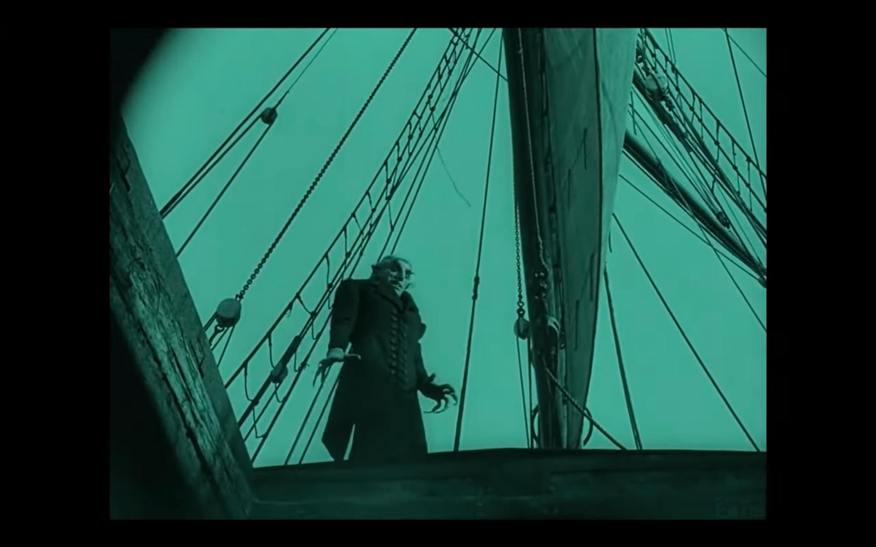 Screenshot aus dem Stummfilm NOSFERATU: Der Vampir Nosferatu, aus der Untersicht aufgenommen, steht auf einem Schiffsdeck.