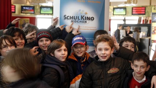 SchulKinoWochen in Hessen: Kinder stehen im Kinofoyer vor einem Plakat der Schulkinowochen