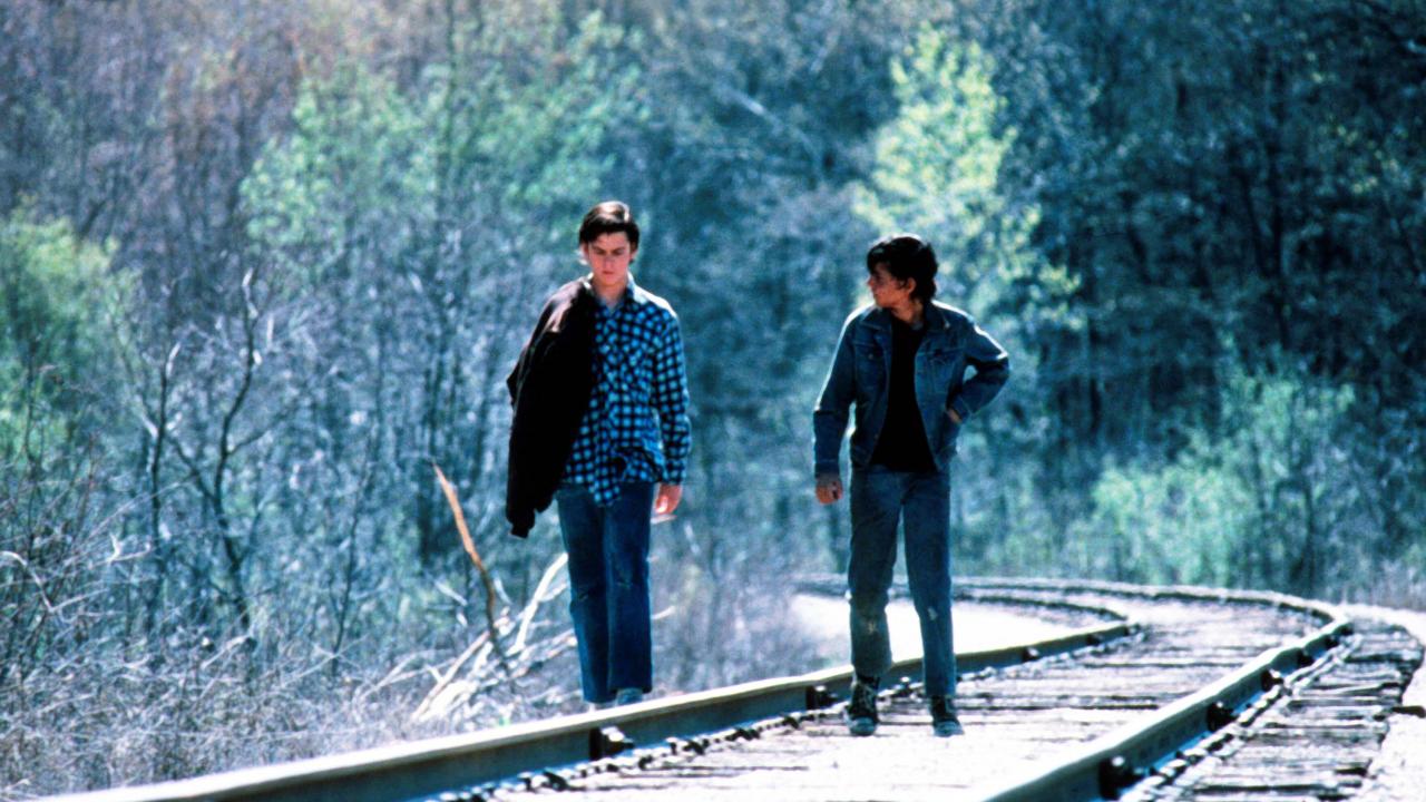 In der Totale: Zwei Jungen im Teenageralter laufen nebeneinander auf Bahngleisen. Die herbstliche Landschaft ist in Blau-Grün-Tönen gehalten.