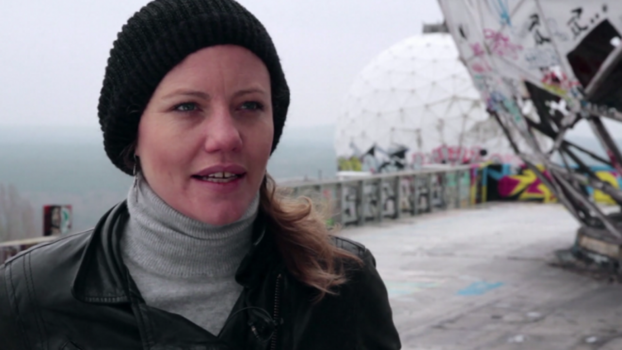 Eine junge Frau mit schwarzer Mütze in Nahaufnahme: sie trägt ein grauen Rollkragenpulli und einer Lederjacke. Sie steht auf der alte Sendestation am Teufelsberg in Berlin. 