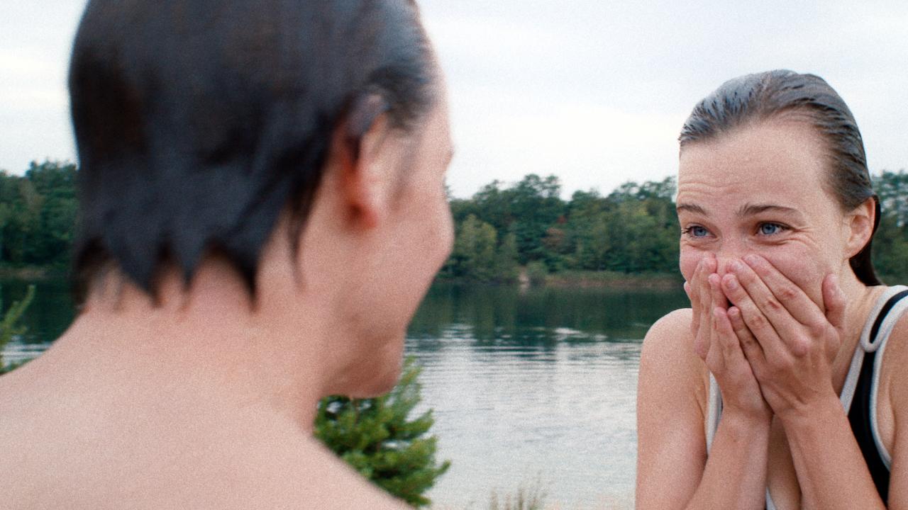 Szenenbild aus dem Film "Fabian oder der Gang vor die Hunde": Ein Mann in der Rückenansicht und eine Frau stehen an einem See. Sie sind beide nass. Die frau hält sich lachend die Hände vor den Mund.