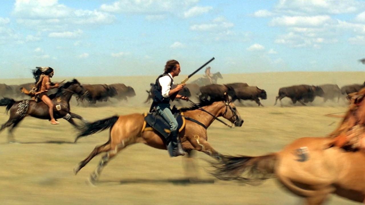 Szenenbild aus dem Western DER MIT DEM WOLF TANZT: Zwei indigene Männer und ein Weißer jagen auf Pferden eine Büffelherde.