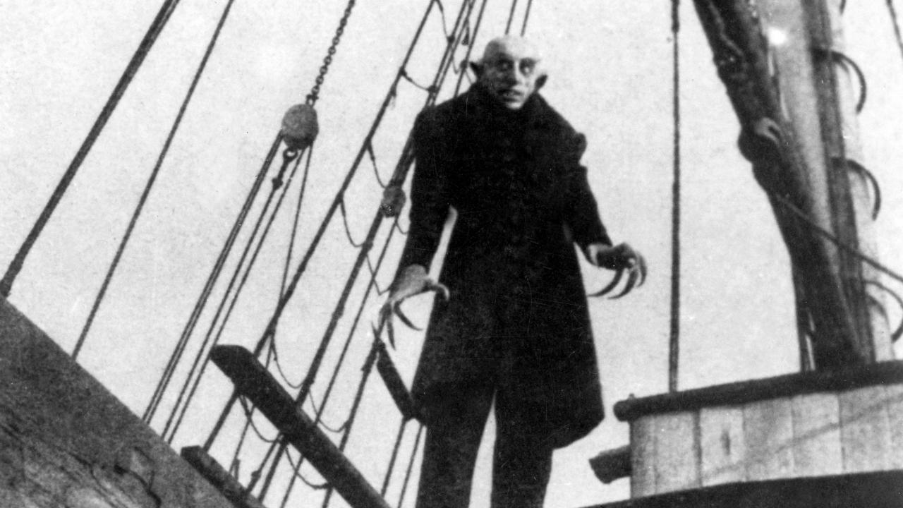 Szenenbild aus dem Stummfilm NOSFERATU - EINE SYMPHONIE DES GRAUENS: Ein unheimlicher Mann mit krallenartigen Fingern steht auf dem Deck eines Segelschiffs