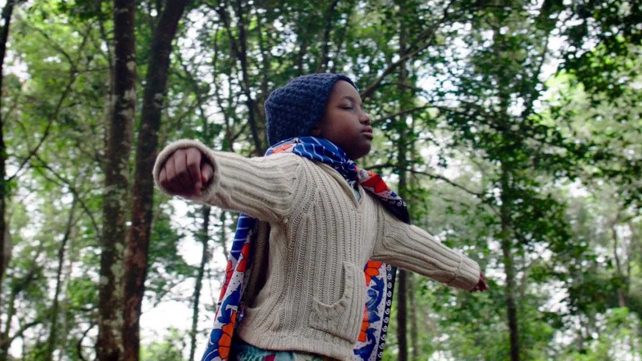 Szenenbild aus dem Film SUPA MODO: Ein Schwarzes Mädchen läuft mit geschlossenen Augen und ausgebreiteten Armen durch einen Wald.