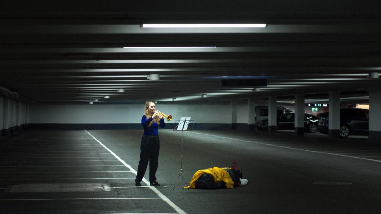 Szenenbild aus dem Film ÜBEN, ÜBEN, ÜBEN: Eine junge Frau steht in einem leeren Parkhaus und spielt Trompete.