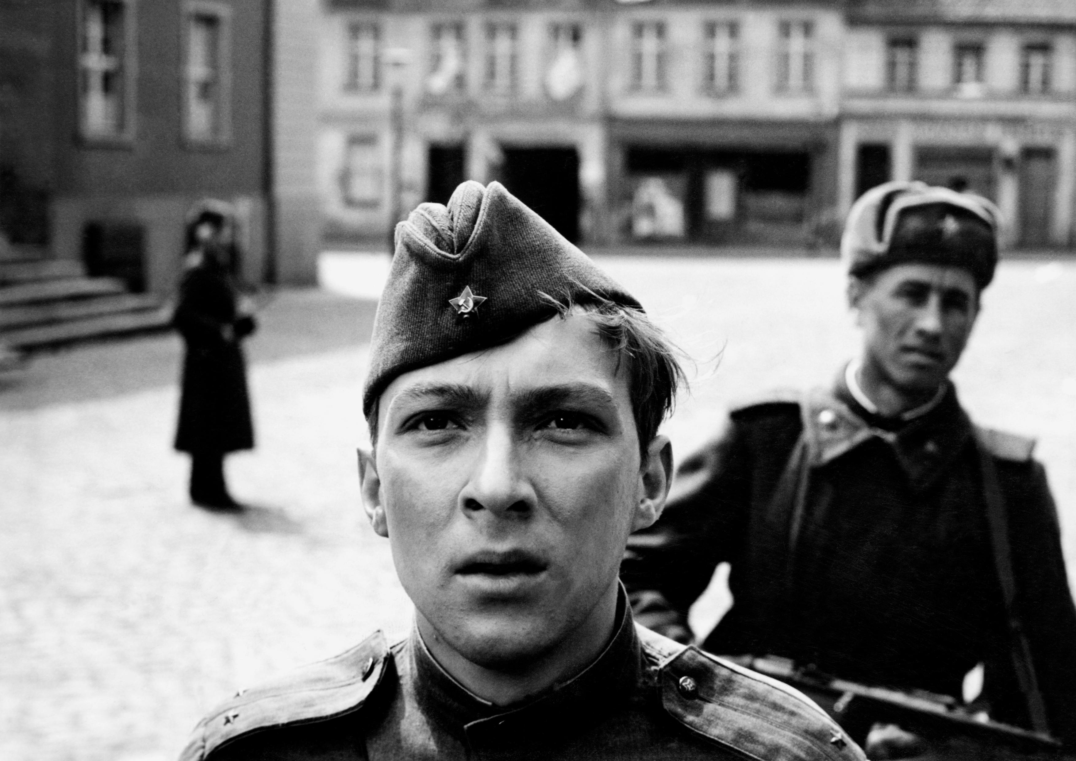 Szenenbild aus dem Film ICH WAR NEUNZEHN: Schwarz-Weiß-Foto zweier junger sowjetischer Soldaten in Uniform während des Zweiten Weltkriegs, einer blickt ernst in die Kamera, der andere steht im Hintergrund.