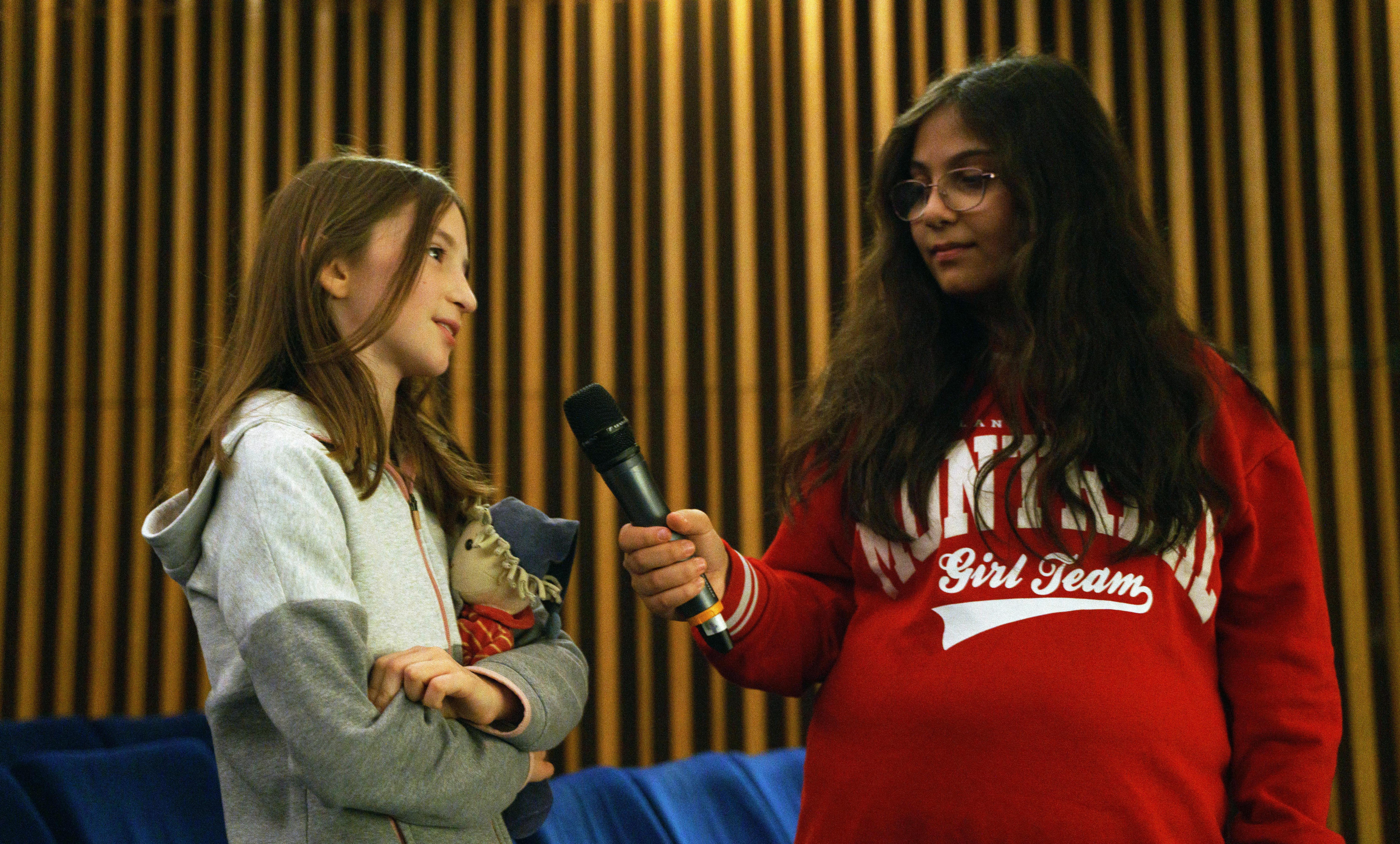 Eröffnung der SchulKinoWochen Berlin 2023 im Kino International: Ein Mädchen im Grundschulalter hält einem etwa gleichaltrigem Mädchen ein Mikrofon hin.