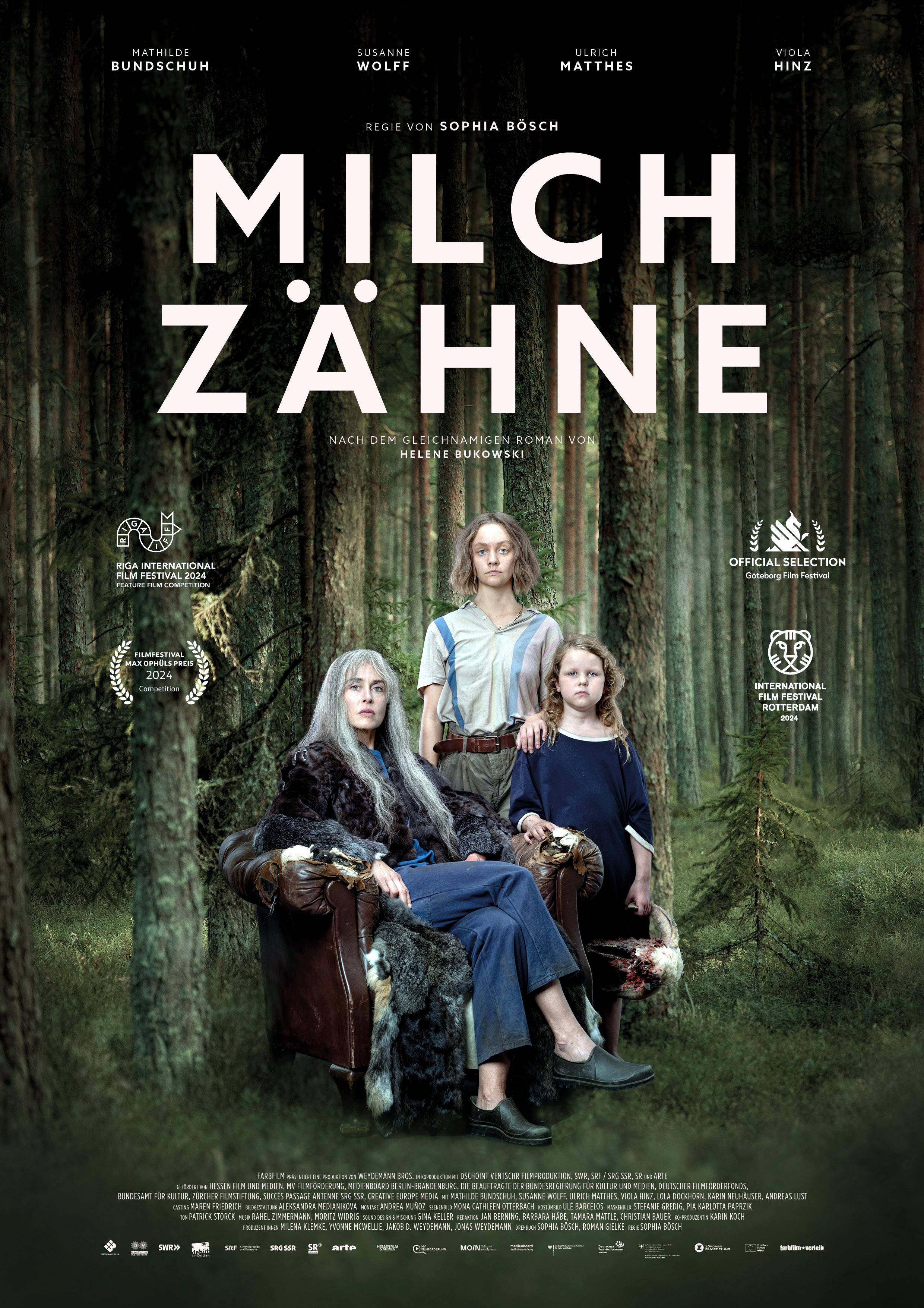 Filmplakat zum Drama MILCHZÄHNE: Vor einer Waldkulisse sitzt eine grauhaarige Frau in einem Sessel. Neben und hinter ihr stehen ein kleines Mädchen und eine junge Frau. Alle schauen ernst in die Kamera. In fetten, weißen Buchstaben steht über der Gruppe der Filmtitel.