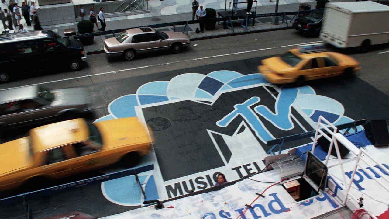 Aufsicht auf die begahrene 6th Avenue in New York. Gelbe Taxis fahren vorbei, sie sind verschwommen. Auf dem Asphalt steht der Schriftzug MTV.