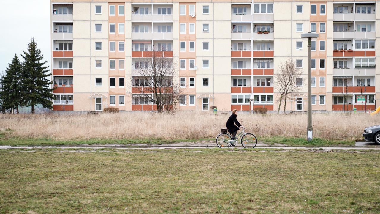 Eine Totale von einer Frau, die auf einem Fahrrad an einem Plattenbau vorbeifährt