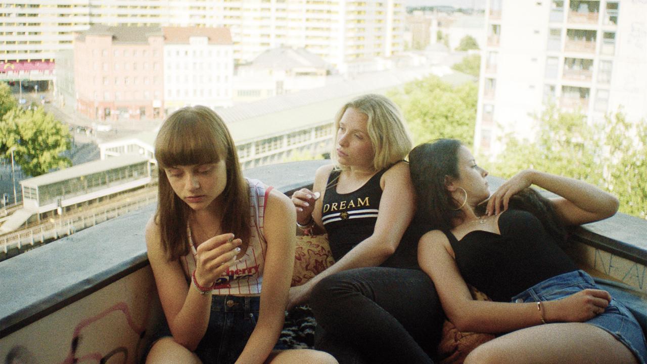 Drei Mädchen im Teenageralte flezen auf einem Balkon. Im Hintegrund ist der Platz Kottbusser Tor in Berlin zu sehen.