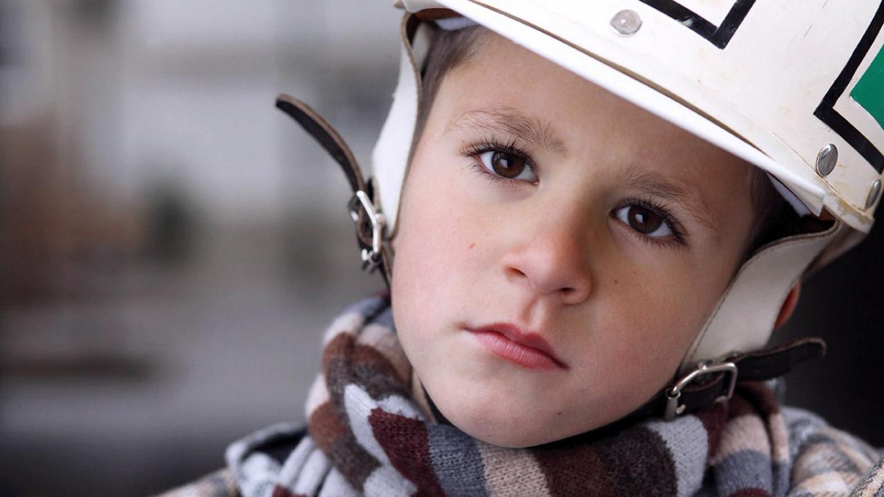 Szenenbild aus dem Film "Das Pferd auf dem Balkon": Großaufnahme eines Jungen, der einen Helm trägt und mit leicht schräg gehaltenem Kopf direkt in die Kamera schaut.