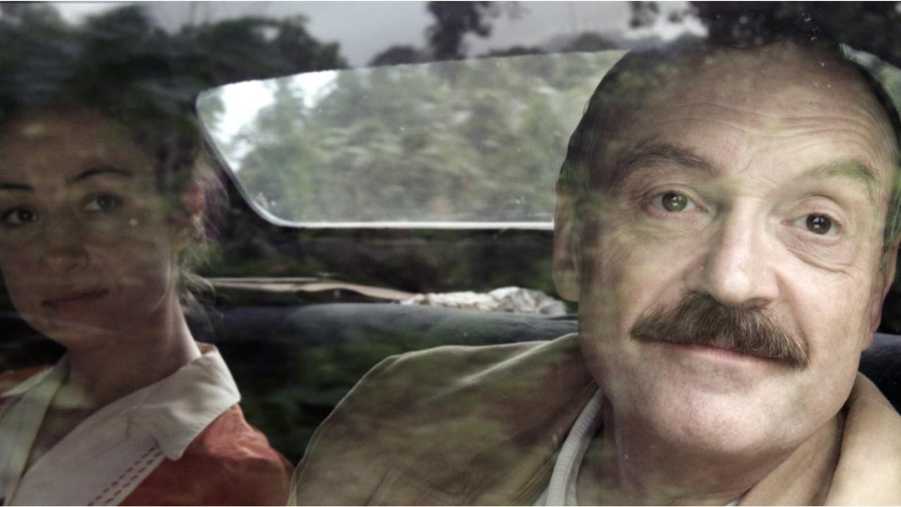 Szenenbild aus dem Biopic "Vor der Morgenröte": Stefan Zweig, gespielt von Josef Hader, blickt lächelnd durch die Seitenscheibe eines Autos. Neben ihm sitzt eine Frau.