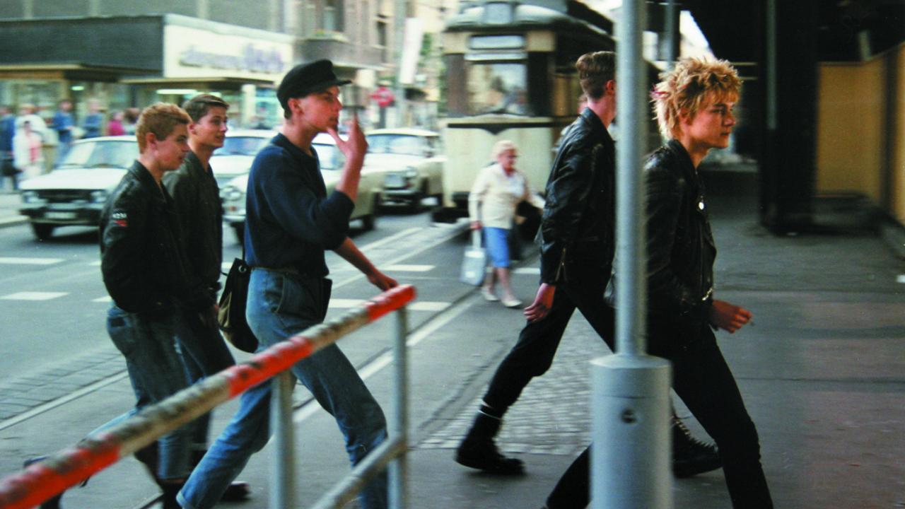 Szenenbild aus dem Dokumentarfilm "flüstern & SCHREIEN": Fünf junge Männer im Punk-Outfit laufen in den späten 1980er-Jahren im Berlin-Prenzlauer Berg über eine Straße.